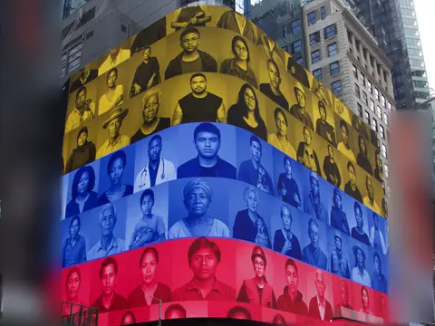 A large wraparound screen above a crosswalk shows the portrait grid in yellow, blue and red.