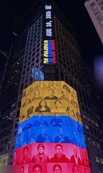 Looking up at a tower at night: a vertical ticker reads Colombia, Aug 10, 2026, above the portrait grid in the colours of the flag.